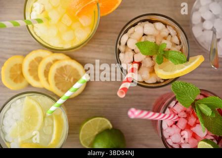 Détail de plusieurs verres avec des boissons gazeuses de différentes saveurs avec de la glace et des pailles sur une table en bois. Vue de dessus. Banque D'Images