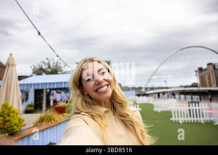 Selfie vue de face d'une femme mi-adulte debout dans une rue du centre-ville, sur un pont à Newcastle, en Angleterre. Elle porte des vêtements décontractés et St Banque D'Images