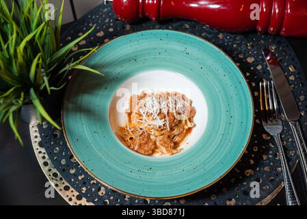 Pâtes tagliatelles fraîchement cuites garnies de sauce salée à la viande bolognaise et de fromage râpé, servies dans une assiette élégante. Banque D'Images