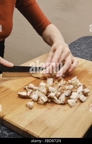 Mains féminines avec couteau coupant le champignon shiitake sur une planche à découper en bois Banque D'Images