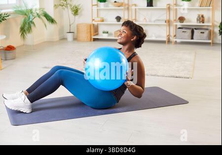 Sportif fit moyen âge femme afro-américaine heureuse faisant de la pratique de fitness à la maison sur tapis Banque D'Images