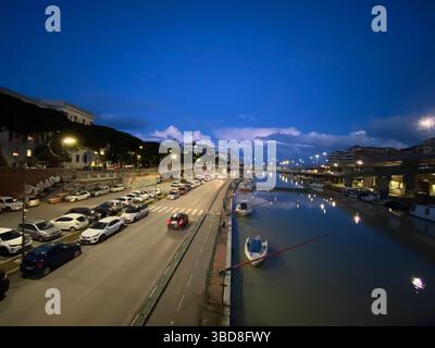 Éclairage urbain du front de mer réfléchissant sur les eaux du canal, véhicules stationnés, bateaux silhouettés pendant le crépuscule du soir à Pescara, en Italie Banque D'Images