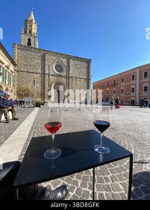 Verres à vin assis sur la table près de la façade de la cathédrale d'Atri, la Piazza Duomo historique qui capture l'élégance architecturale italienne dans la région des Abruzzes Banque D'Images