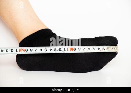 Pied féminin en chaussette et ruban à mesurer sur fond blanc, mesurant la longueur du pied pour déterminer la taille de la chaussure pour un adulte Banque D'Images