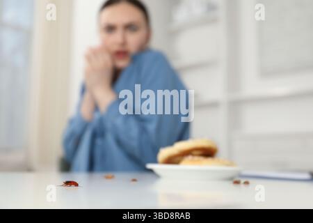 Jeune femme choquée regardant des cafards et des bretzels sur une table blanche à l'intérieur, mise au point sélective. Problème de ravageur Banque D'Images