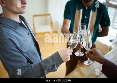 Vue rapprochée de trois personnes qui tapissent des verres de champagne en fête dans un cadre intérieur lumineux avec parquet Banque D'Images