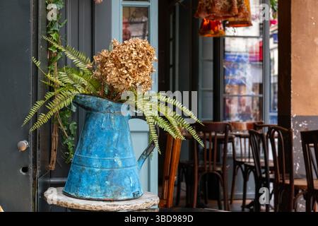 Une cruche en métal bleu utilisée comme vase dans un café. Banque D'Images
