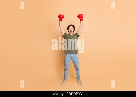 Jeune homme portant une tenue décontractée célébrant avec poings relevés et gants de boxe sur fond beige Banque D'Images