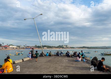Bali, Indonésie - 22 décembre 2024 : un groupe de personnes est assis sur un quai au bord de l'eau. Le ciel est nuageux et l'eau est calme Banque D'Images