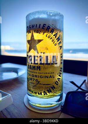 Grand verre de bière estrella avec condensation sur une table avec une vue sur la plage et l'océan en arrière-plan, Banque D'Images