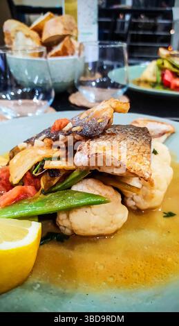 Plat gastronomique de filet de poisson poêlé avec légumes rôtis, chou-fleur et coin de citron, servi dans un bouillon. Repas gastronomique maison sur un dîner Banque D'Images