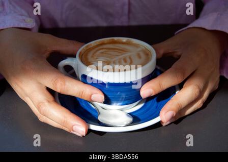 Mains tenant une tasse de café. Cappuccino dans une tasse bleue. Une femme avec une tasse de café dans les mains. Banque D'Images