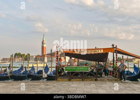 Gondoliers dans un moment de pause au quai des gondoles de Riva degli Schiavoni, avec l'île de San Giorgio Maggiore en arrière-plan, Venise Banque D'Images