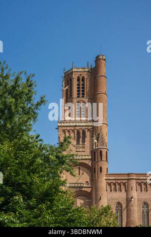 La grande tour de briques s'élève au-dessus de la cathédrale Sainte-Cécile à Albi, en France, contre un ciel bleu clair et des arbres verts au premier plan. Banque D'Images