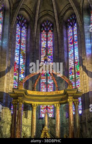Des vitraux remplissent les absides incurvées de l'église Saint Salvi à Albi, en France, projetant une lumière colorée sur l'autel doré orné du chœur. Banque D'Images