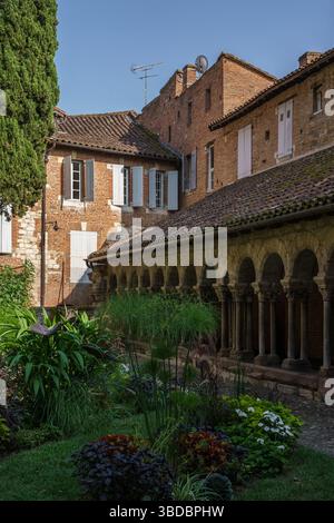 La lumière du soleil brille à travers les arches et les cyprès dans le cloître médiéval Saint Salvi à Albi, en France, créant une retraite paisible et verdoyante près de l'ancienne wa Banque D'Images