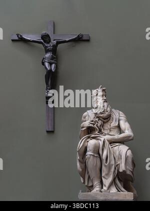 Londres, Royaume-Uni - 07 mai 2025 - Statue en marbre de Moïse par Michel-Ange avec la figure frappante de Jésus Christ crucifié sur la croix dans le mur vert b Banque D'Images