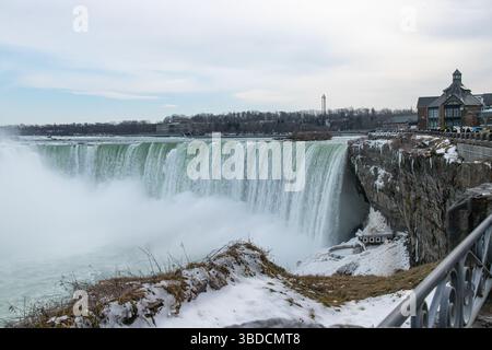 Vue détaillée des chutes Horseshoe (chutes du Niagara) en hiver, avec la brume montante, les environs glacés et les bâtiments à proximité sous un ciel nuageux. Banque D'Images