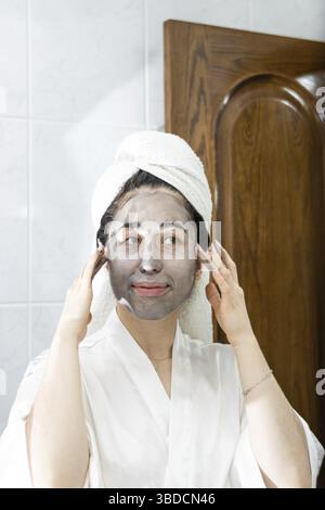 Jeune femme regardant dans le miroir tout en appliquant le produit de beauté à la maison Banque D'Images