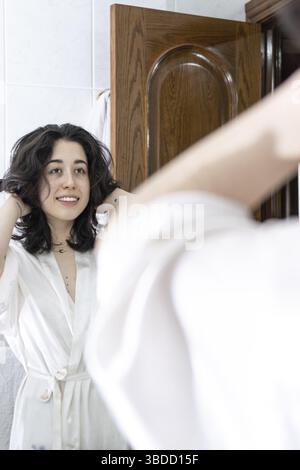 Femme heureuse dans la salle de bain. Jeune femme jouant avec ses cheveux devant un miroir Banque D'Images