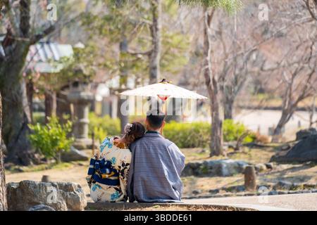 Couple à Kimono profitant d'un moment de paix dans un parc japonais, homme tenant un parapluie japonais Wagasa. Kyoto, Japon. Banque D'Images