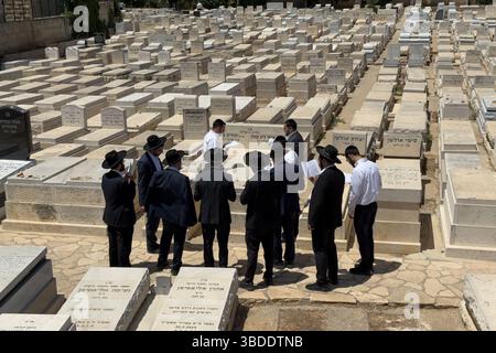 Hommes juifs religieux ultra orthodoxes priant sur une tombe dans le cimetière de Sanhedria cimetière juif situé dans le quartier de Sanhedriya, à proximité de logements résidentiels. Jérusalem-Ouest Banque D'Images