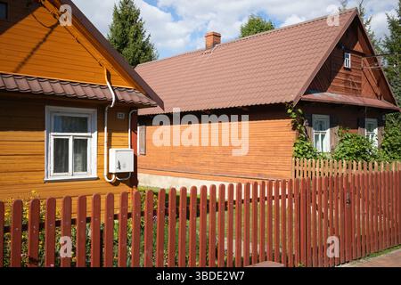 Deux maisons avec des toits bruns et des clôtures en bois devant eux. Une maison est peinte en orange. La clôture est en bois et a une couleur rouge Banque D'Images