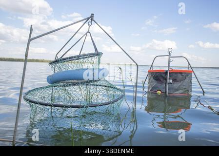 Deux enclos de pêche sont fixés au sol sous l'eau d'un barrage parmi la végétation avec l'eau du barrage et des nuages blancs parmi le ciel bleu dedans Banque D'Images