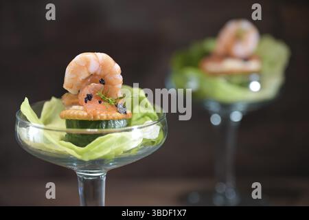 Apéritif ou collation de fête avec saumon, crevettes et caviar sur laitue servi dans un verre à cocktail sur un fond sombre pour des vacances comme Noël et Banque D'Images