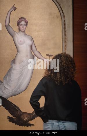 Sur cette image, nous voyons une personne aux cheveux bouclés, portant un haut de couleur foncée et un Jean de couleur claire, debout devant une peinture. Le tableau Banque D'Images