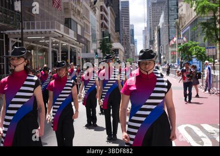 Une fanfare, majoritairement féminine, en uniforme rose, noir et bleu vif, défilés dans une rue de la ville. Les grands bâtiments et les spectateurs bordent le b. Banque D'Images