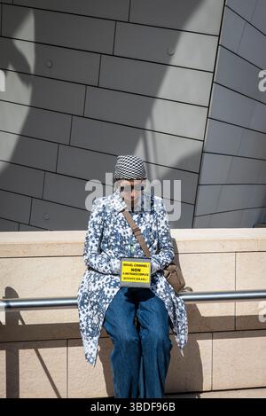 Femme musulmane qualifiant Israël de criminel assise devant la Fondation Louis Vuitton, Paris, France Banque D'Images