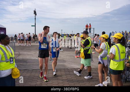 Les coureurs en bleu et jaune s'habillent sur une promenade après une course, recueillant les médailles des bénévoles dans des gilets de sécurité jaune vif. Spectateurs et St Banque D'Images