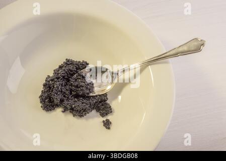 Une assiette en céramique blanche sur une table en bois avec du caviar noir et une cuillère en argent trempée dans le caviar Banque D'Images
