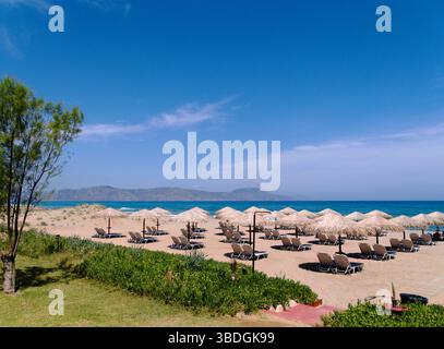 Plage idyllique d'Episkopi, Réthymnon, Crète, Grèce. Chaises longues en rangées sur le sable doucement rayé. Scène estivale grecque typique. Banque D'Images