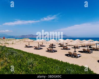 Belle plage d'Episkopi, Rethymnon, Crète, Grèce. Chaises longues en rangées sur le sable doucement rayé. Scène estivale grecque typique. Banque D'Images
