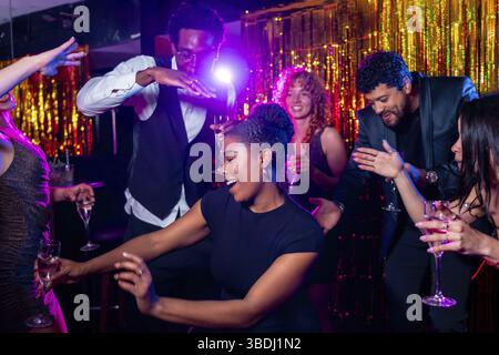 Joyeux amis multi-ethniques dansant et buvant du champagne, profitant de la vie nocturne animée à la discothèque Banque D'Images