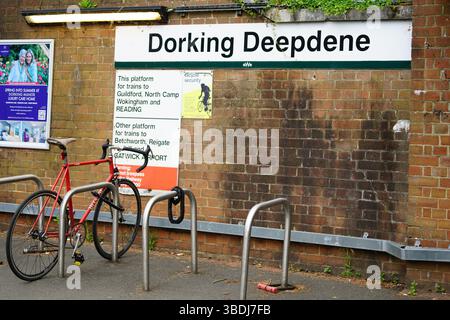 Vélo rouge fixé à des supports métalliques devant un panneau de gare "Dorking Deepdene". Dorking, Royaume-Uni Banque D'Images