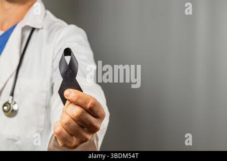 Un travailleur de la santé vêtu d’un manteau blanc arbore un ruban noir comme symbole de souvenir et de solidarité. Le réglage est neutre et souligne le signi Banque D'Images