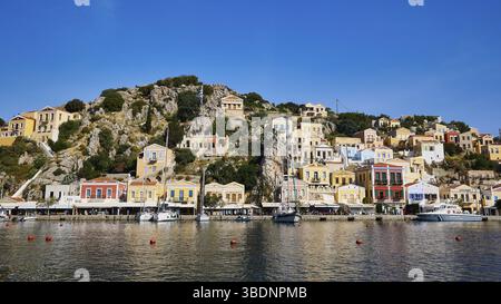 Des maisons colorées bordent une ville côtière au bord de l'eau, des bateaux de pêche reposent à l'ancre, Symi Town, Symi, Dodécanèse, îles grecques, Grèce, Europe Banque D'Images