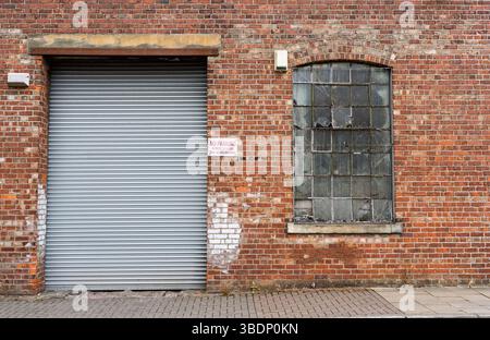 Bâtiment industriel avec une façade en brique avec une grande porte de sécurité en métal et une fenêtre couverte de mess de fil usé Banque D'Images