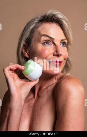 Portrait de beauté de belle femme mature, concepts sur les cosmétiques, les soins de la peau et le bien-être. Femme mature souriante appliquant la crème cosmétique dans un stu chaud Banque D'Images