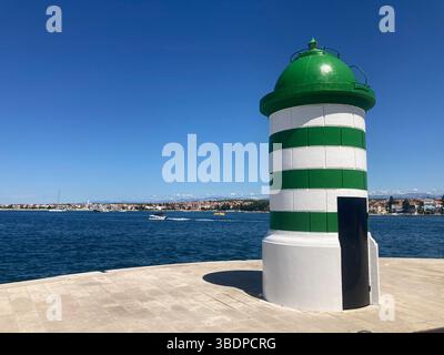 Petit phare vert sur le quai de Zadar, utilisé pour la navigation maritime et l'amarrage dans le port côtier animé de l'Adriatique Banque D'Images