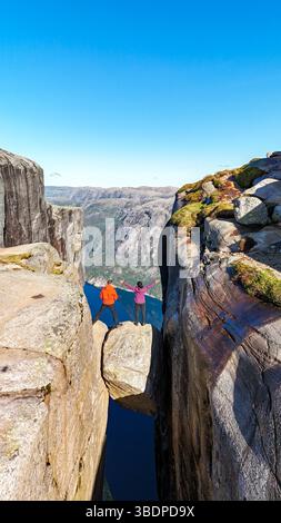 Deux aventuriers se tiennent sur une corniche rocheuse étroite, entourée de falaises majestueuses et de fjords profonds du Kjeragbolten Lysefjord, en Norvège Banque D'Images