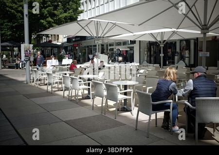 La photo montre un café en plein air avec des chaises en osier blanc et des tables sous de grands parasols blancs. Les gens sont assis aux tables, appréciant la journée. I Banque D'Images