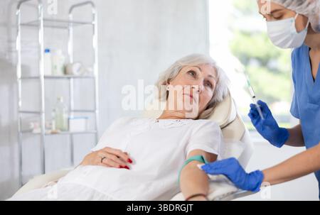 Femme médecin faisant l'injection à la vieille femme fatiguée endormie dans la clinique. Banque D'Images
