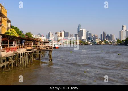 Bangkok, Thaïlande. 05 mars 2025. Structures traditionnelles en bois vues à côté de la rivière Chao Phraya avec la ligne d'horizon moderne de la ville de bureaux et d'immeubles d'appartements de grande hauteur. (Photo de John Wreford/SOPA images/SIPA USA) crédit : SIPA USA/Alamy Live News Banque D'Images