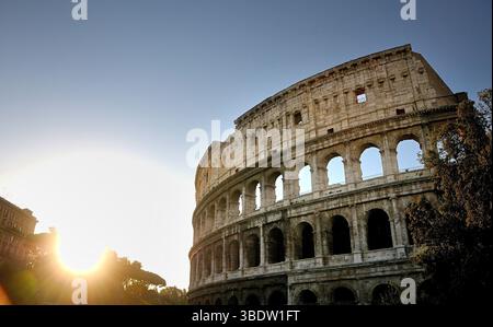 Le Colisée se dresse majestueusement contre un soleil couchant, soulignant son ancienne structure en pierre et ses entrées voûtées. Rome. Italie Banque D'Images