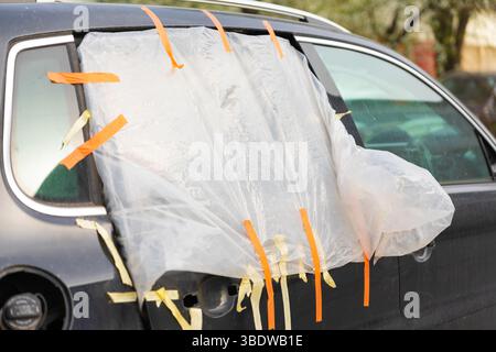 Vitre arrière de voiture endommagée temporairement recouverte de feuille de plastique et de ruban adhésif, servant de solution rapide pour la protection contre les intempéries. Banque D'Images