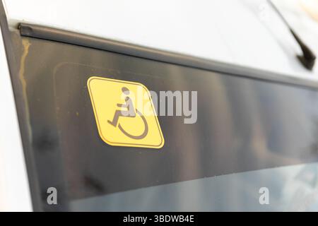 Gros plan d'un autocollant jaune d'accessibilité pour fauteuil roulant sur la vitre d'un véhicule, indiquant l'accès aux transports pour les personnes handicapées. Banque D'Images